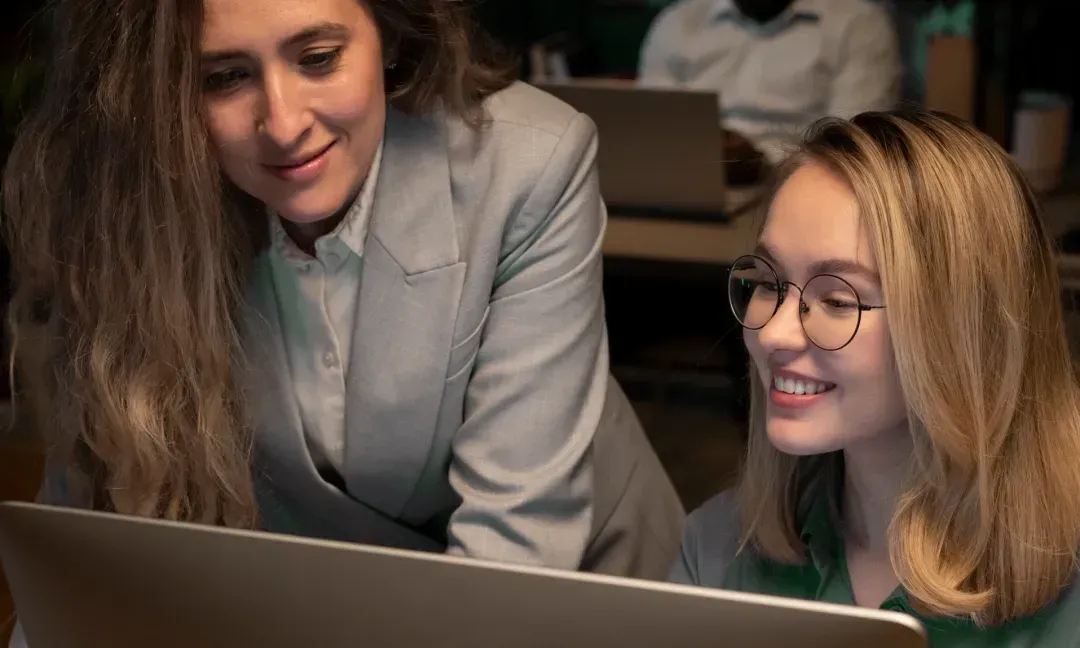 Two women smiling as they look at a laptop together