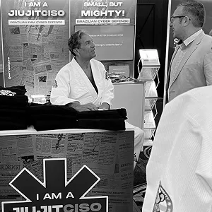 Man in a white gi talking with a visitor at the “I am a JiujitCISO” booth