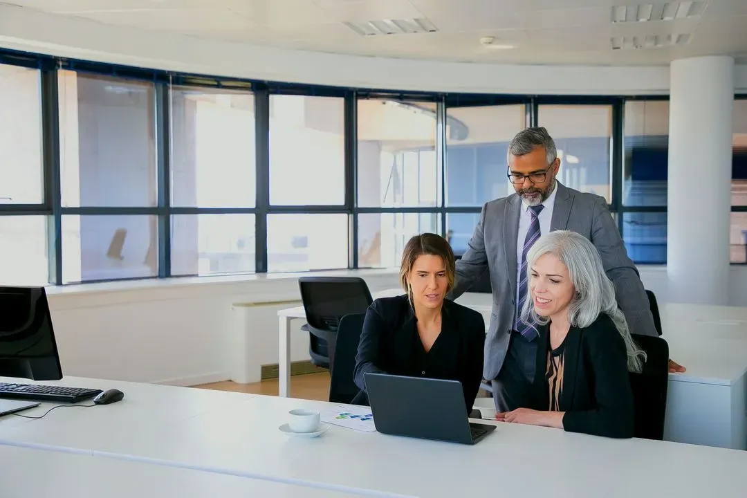 Three colleagues reviewing something on a laptop in a bright, open office