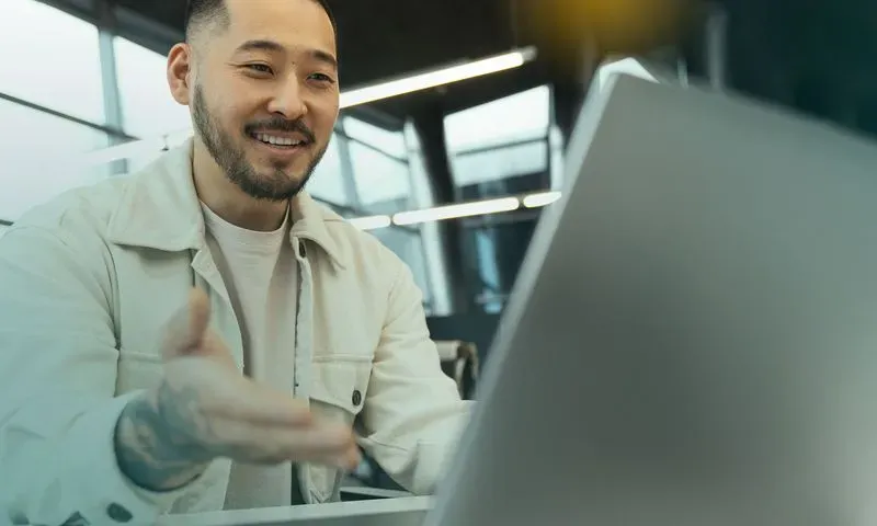 Smiling man gesturing toward his laptop
