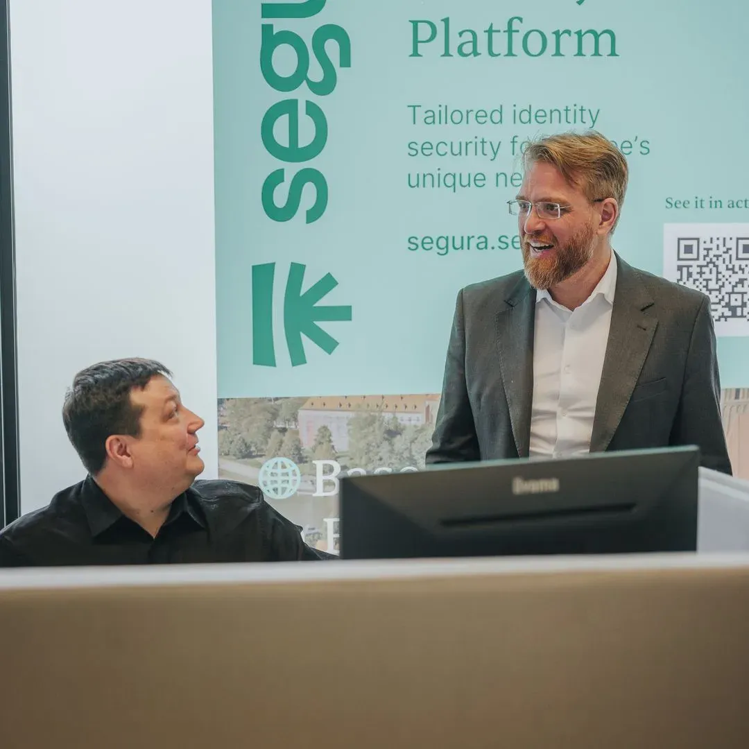 Two professionals talking at a workstation in front of a Segura™ poster