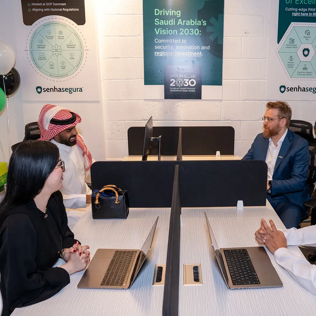 Team talking at workstations beneath posters about Saudi Arabia’s Vision 2030