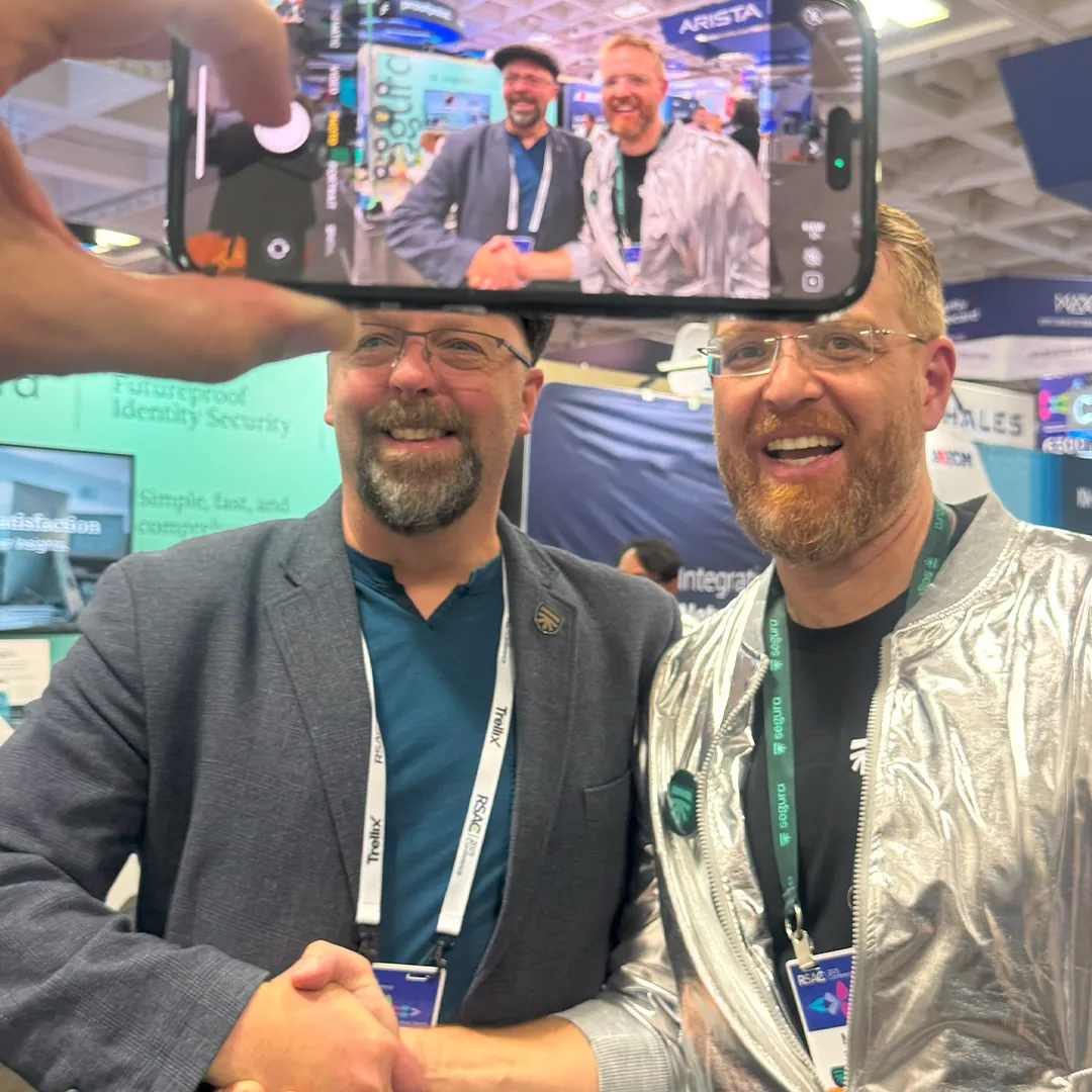 Two men shaking hands at the Segura™ booth while someone films them on a phone