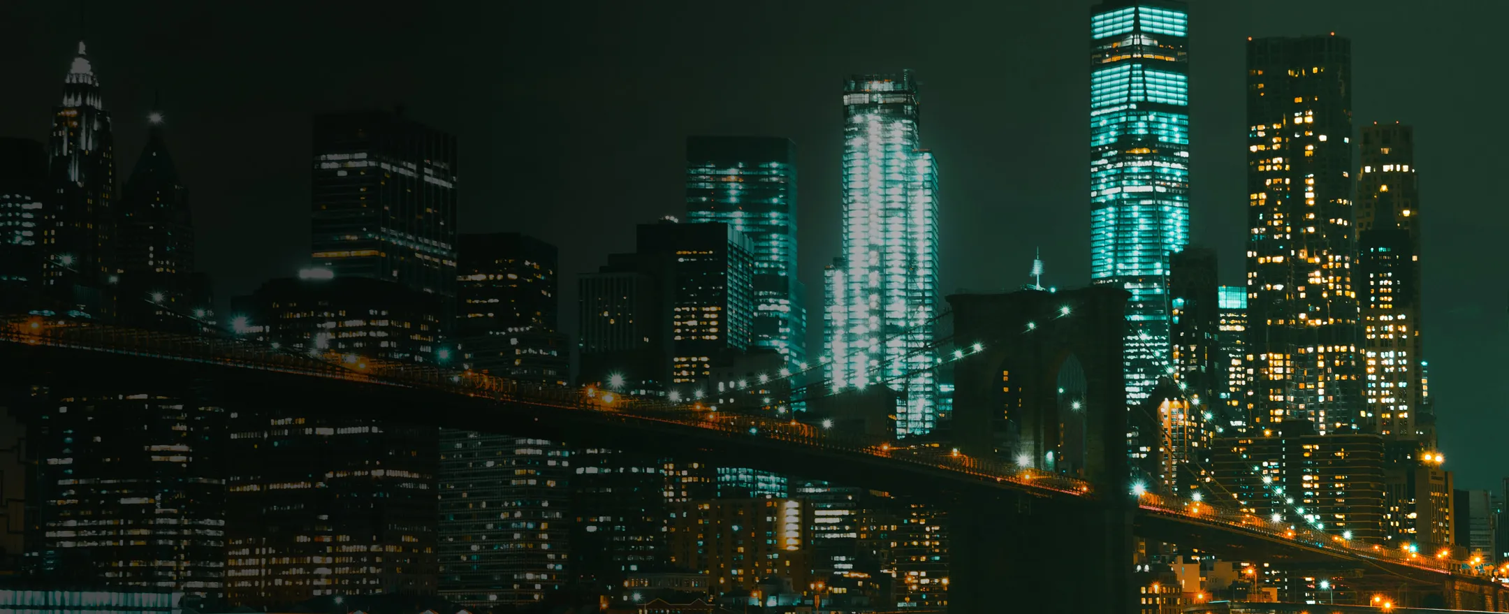 New York skyline at night with the lit Brooklyn Bridge.