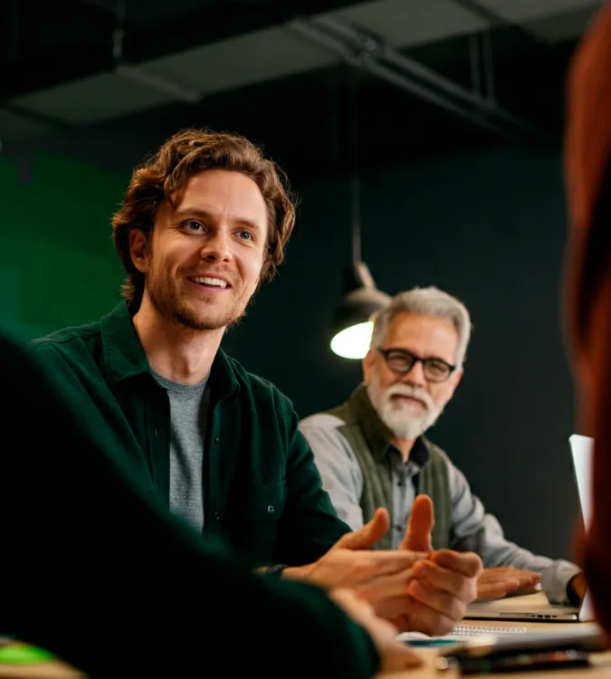 Smiling man talking with colleagues around a meeting table
